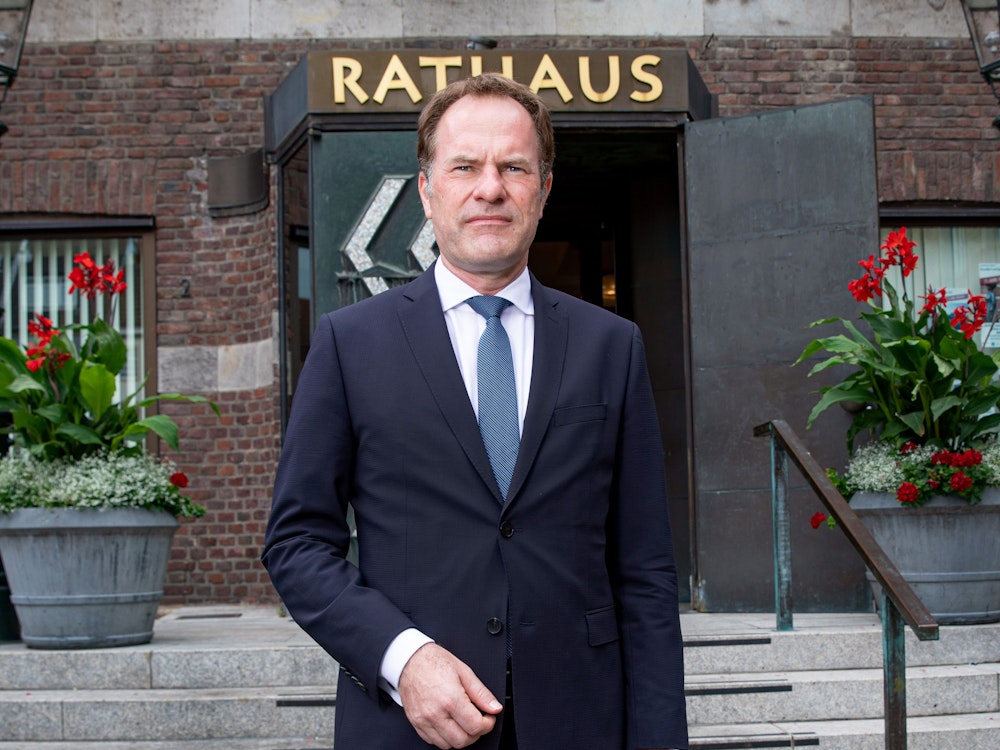 Stephan Keller, Oberbürgermeister von Düsseldorf, trägt einen Anzug und posiert vor dem Eingang zum Rathaus.
