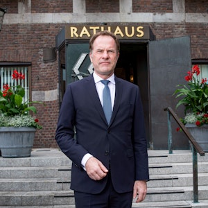 Stephan Keller, Oberbürgermeister von Düsseldorf, trägt einen Anzug und posiert vor dem Eingang zum Rathaus.