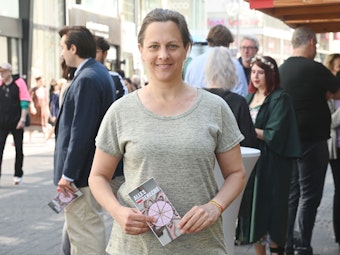 Nicolin Gabrysch steht mit einem Wahlzettel in der Hand in Köln auf der Straße und lächelt in die Kamera.