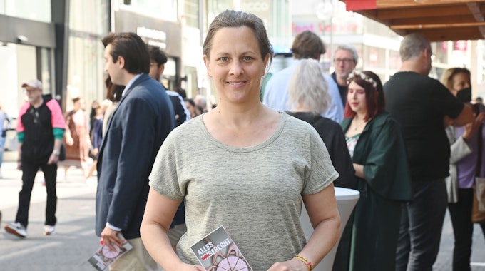 Nicolin Gabrysch steht mit einem Wahlzettel in der Hand in Köln auf der Straße und lächelt in die Kamera.