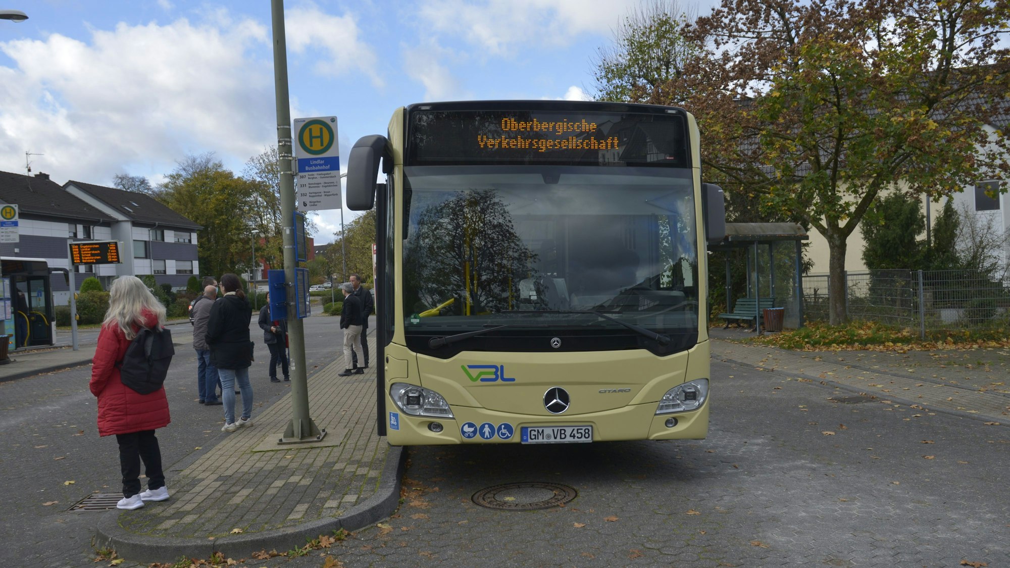 Ein gelber Bus steht an einer Haltestelle. Personen sind im Hintergrund zu sehen.