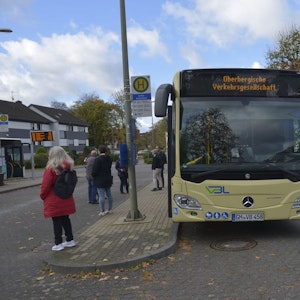 Ein gelber Bus steht an einer Haltestelle. Personen sind im Hintergrund zu sehen.