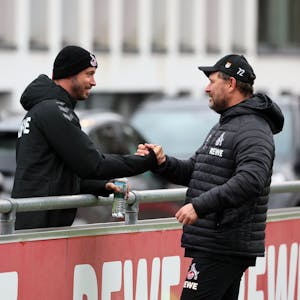 Kölns verletzter Offensivspieler Mark Uth (l.), der eine schwarze Mütze trägt, begrüßt FC-Coach Steffen Baumgart am Rande der Trainingseinheit.
