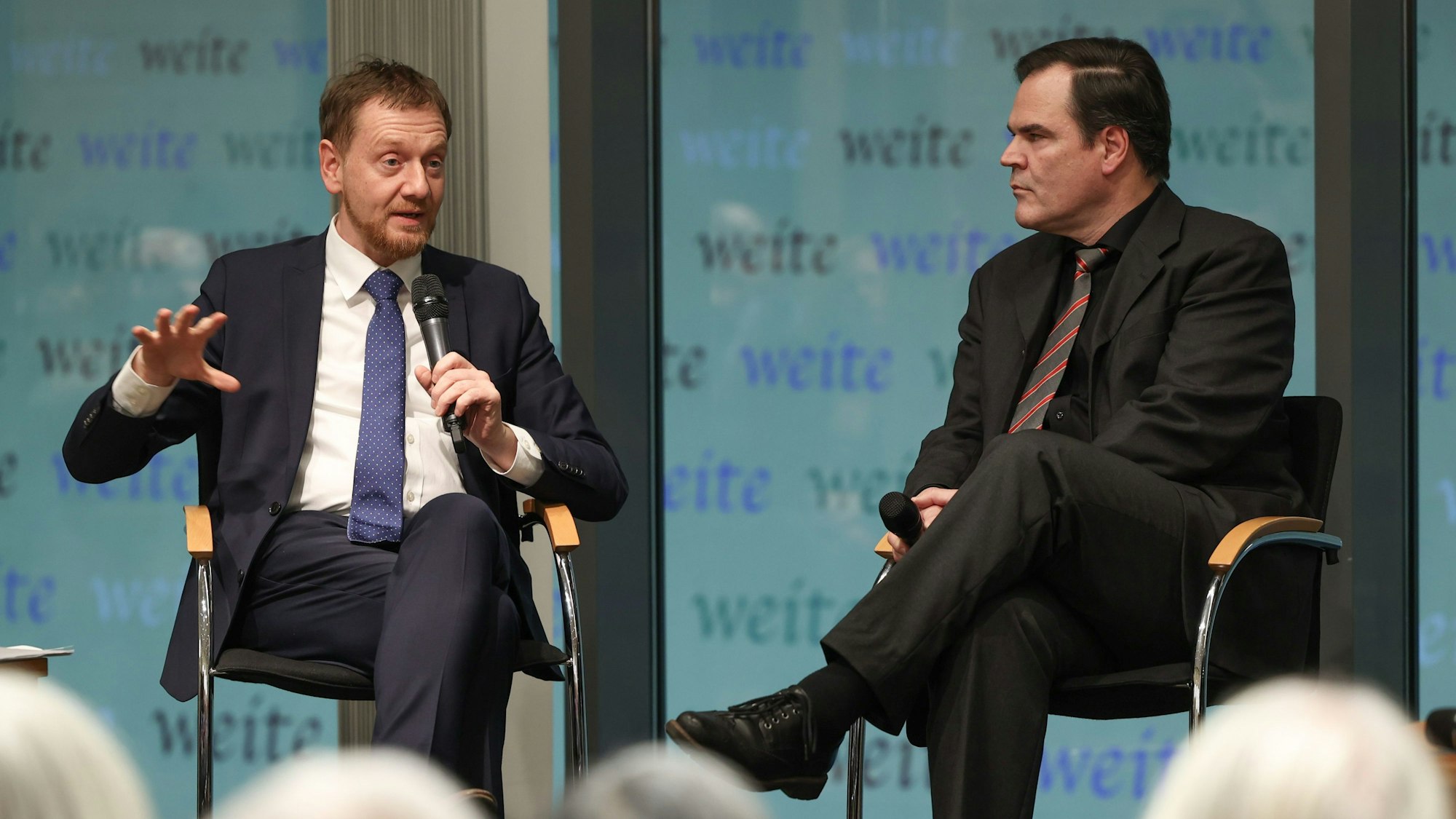 Sachsens Ministerpräsident Michael Kretschmer (l, CDU) und Autor Uwe Tellkamp sitzen bei einer Lesung in der Landesvertretung Sachsens auf der Bühne.