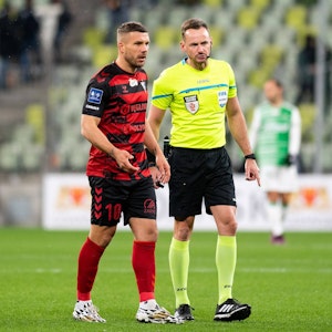 Lukas Podolski im Auswärtstrikot von Gornik Zabrze neben Schiedsrichter Pawel Raczkowski.