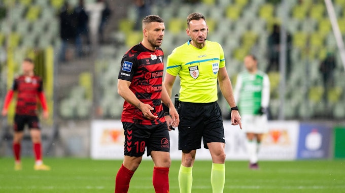 Lukas Podolski im Auswärtstrikot von Gornik Zabrze neben Schiedsrichter Pawel Raczkowski.