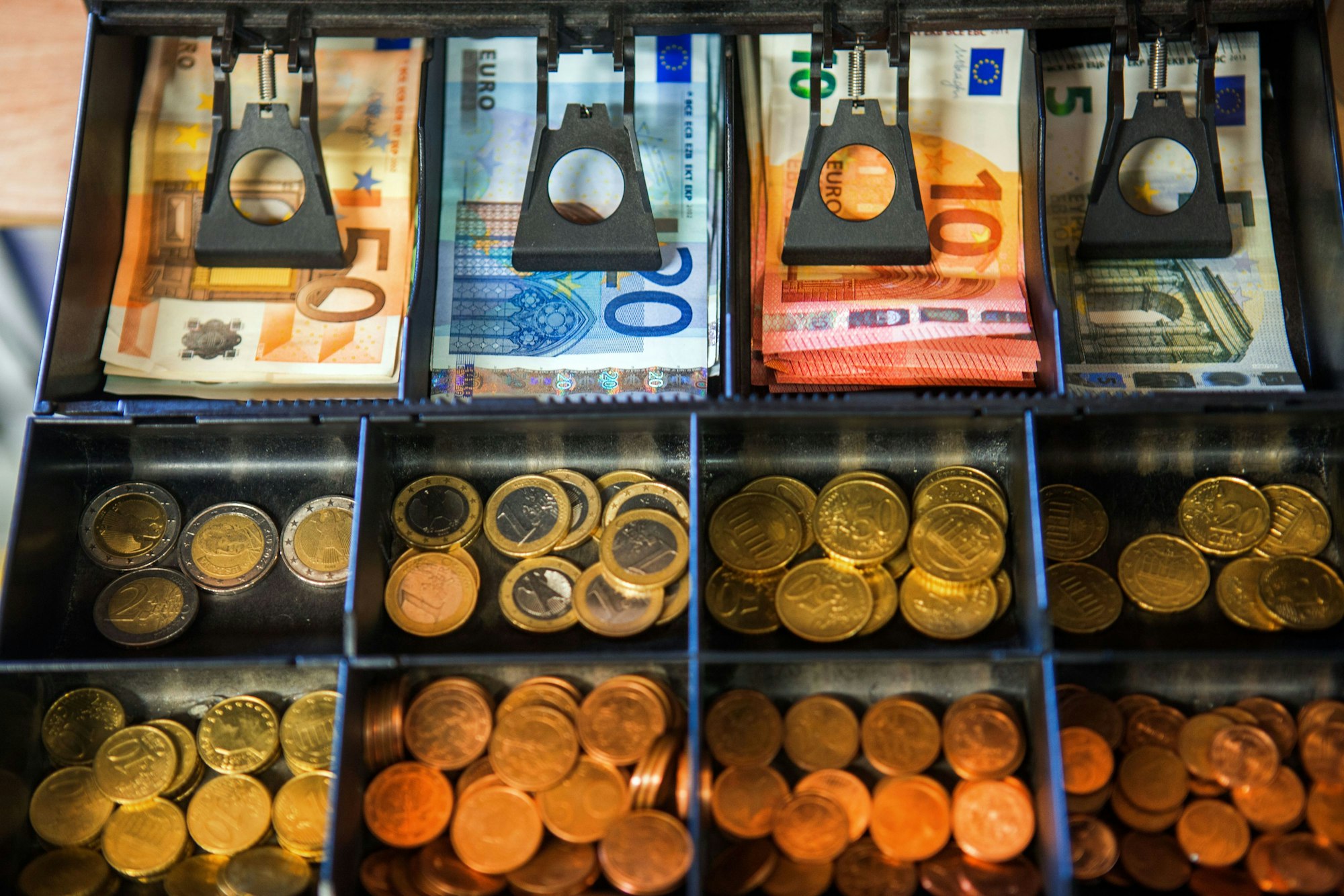 Das Geldfach einer Ladenkasse mit Münzen und Scheinen darin.
