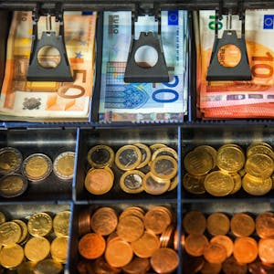Das Geldfach einer Ladenkasse mit Münzen und Scheinen darin.