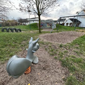 Ein leerer Spielplatz in Niederkassel. Im Vordergrund ist eine Wippe für eine Person, die die Form eines Esels hat. Im Hintergrund sind Schaukeln und Reifen.