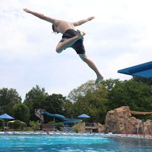 Ein junger Mann springt von einem Sprungbrett ins Becken des Freibades auf Grafenwerth. Im Hintergrund ist eine große Rutsche zu sehen.