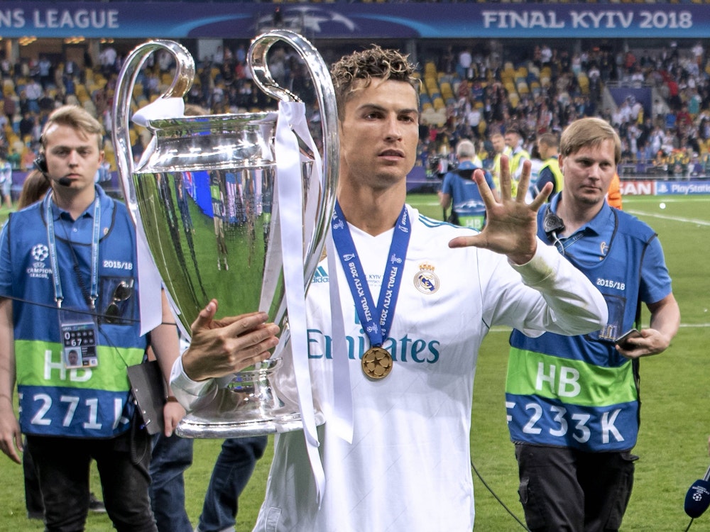 Cristiano Ronaldo hält den Champions-League-Pokal in der Hand und zeigt mit der anderen Hand eine fünf.