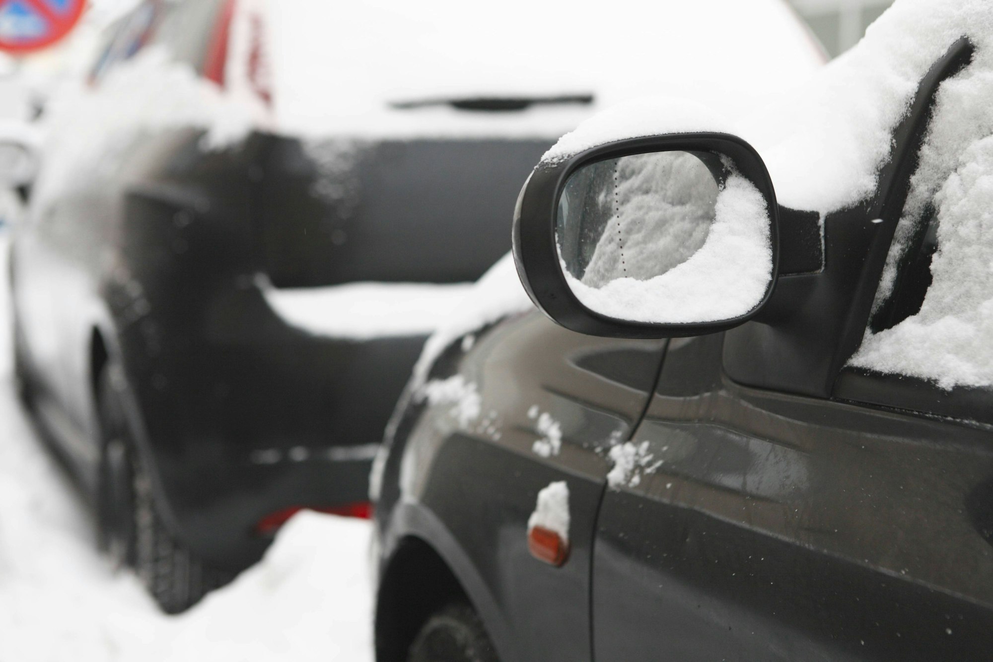 Symbolfoto. Außenspiegel an einem schwarzen, parkenden Auto mit Schnee.
