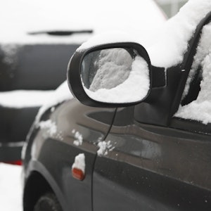 Symbolfoto. Außenspiegel an einem schwarzen, parkenden Auto mit Schnee.