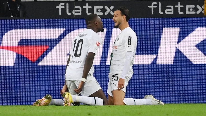 Ramy Bensebaini (r.) und Marcus Thuram bejubeln Bensebaini Treffer zum 3:0 für Borussia Mönchengladbach gegen RB Leipzig am 17. September 2022. Beide Spieler sitzen sich auf den Knien gegenüber und lachen sich an.