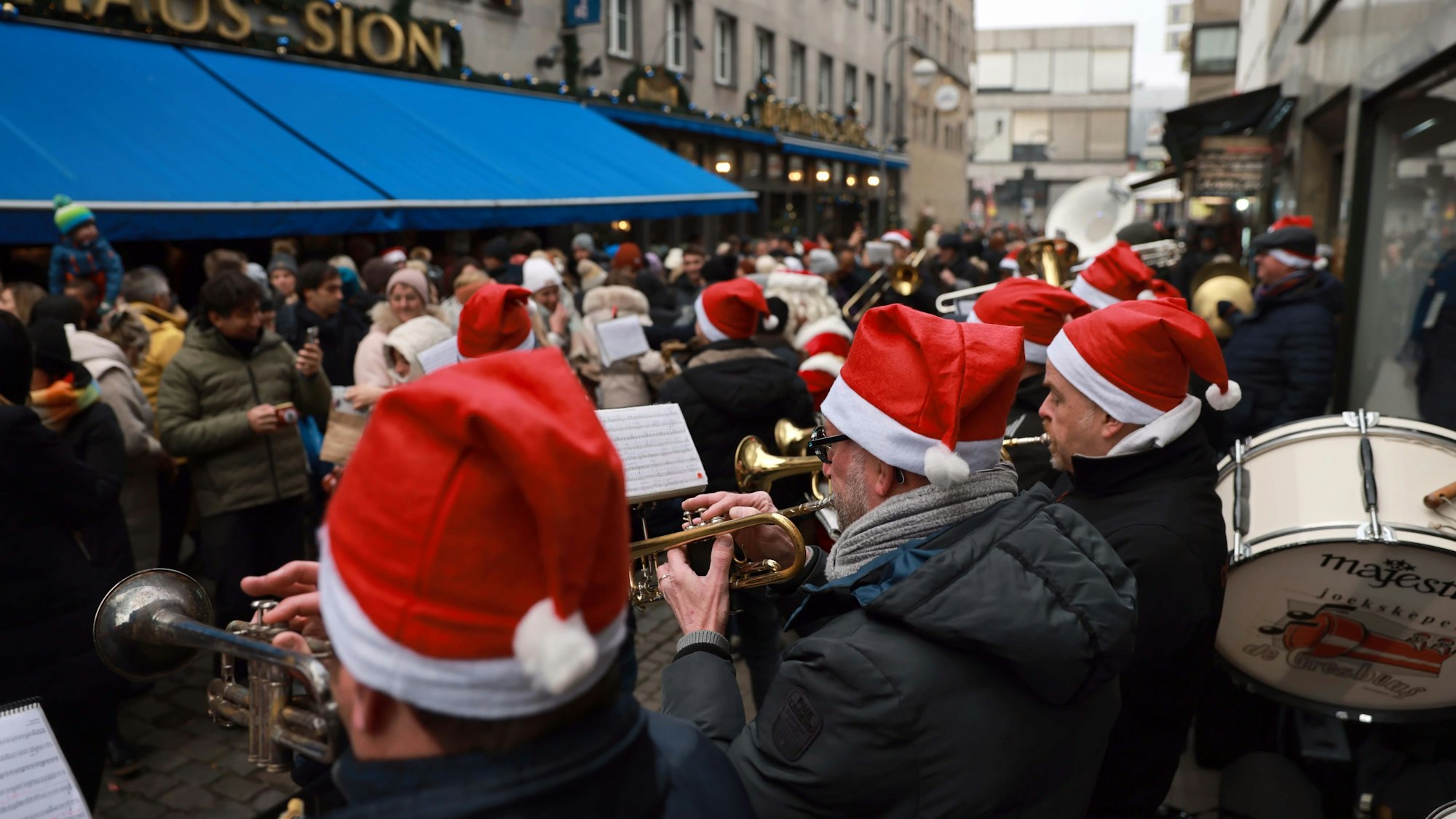 Menschen mit Weihnachtsmützen spielen Trompete vor einem Brauhaus.