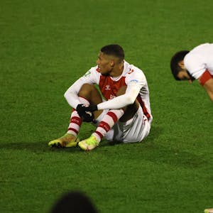 Ein Fußballspieler sitzt nach einer Niederlage enttäuscht auf dem Rasen, ein anderer stützt die Hände auf die Knie.&nbsp;
