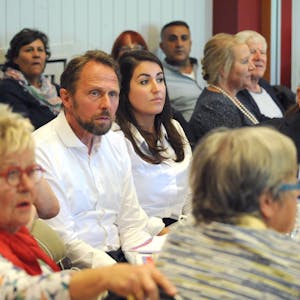 Leverkusens Oberbürgermeister sitzt während einer Veranstaltung neben seiner engsten Vertrauten und Büroleiterin Aylin Doğan. Beide schauen ernst.