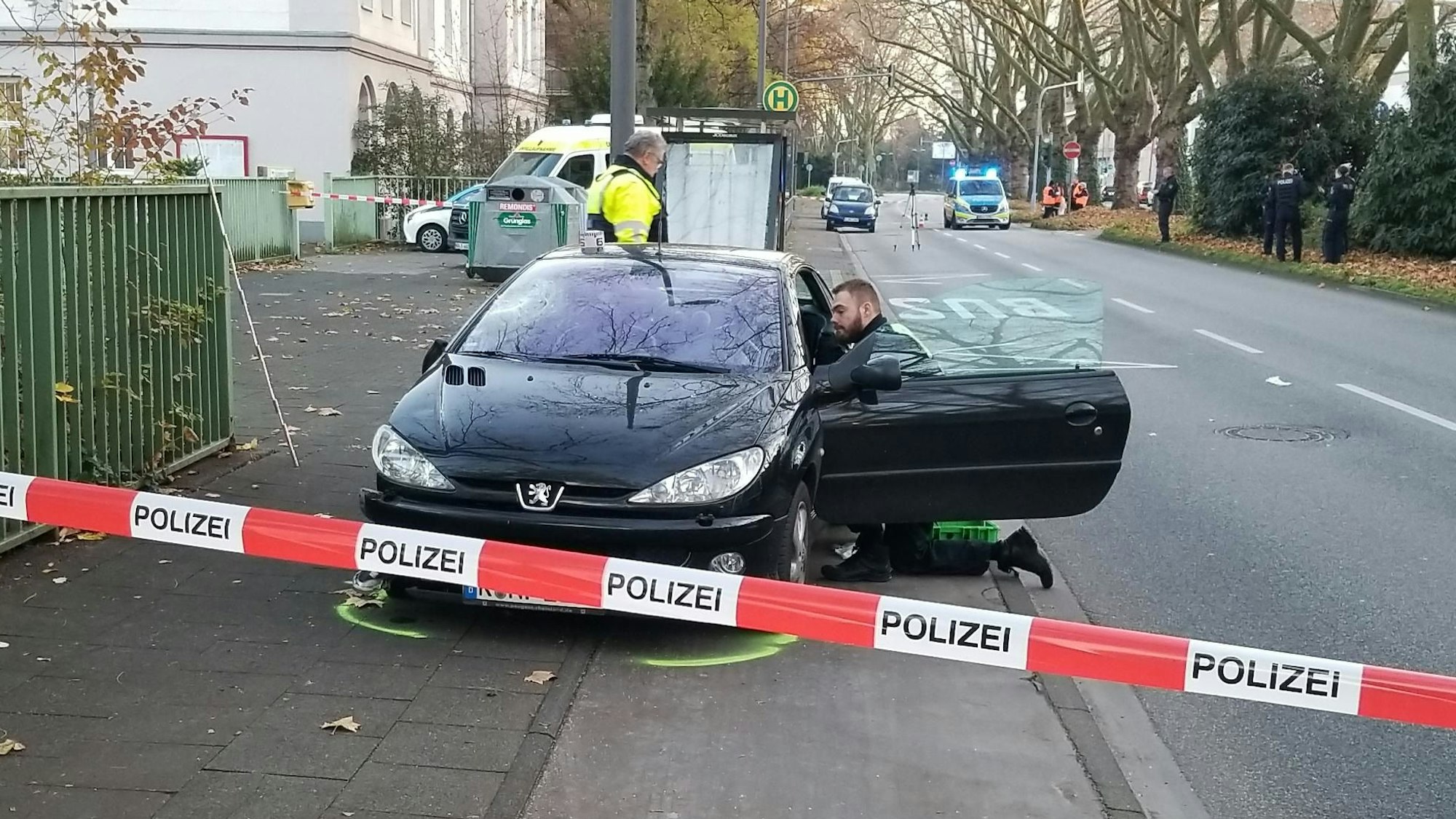 Flatterband sperrt eine Straße ab, ein Polizist kniet in der offenen Tür eines verunglückten Autos.