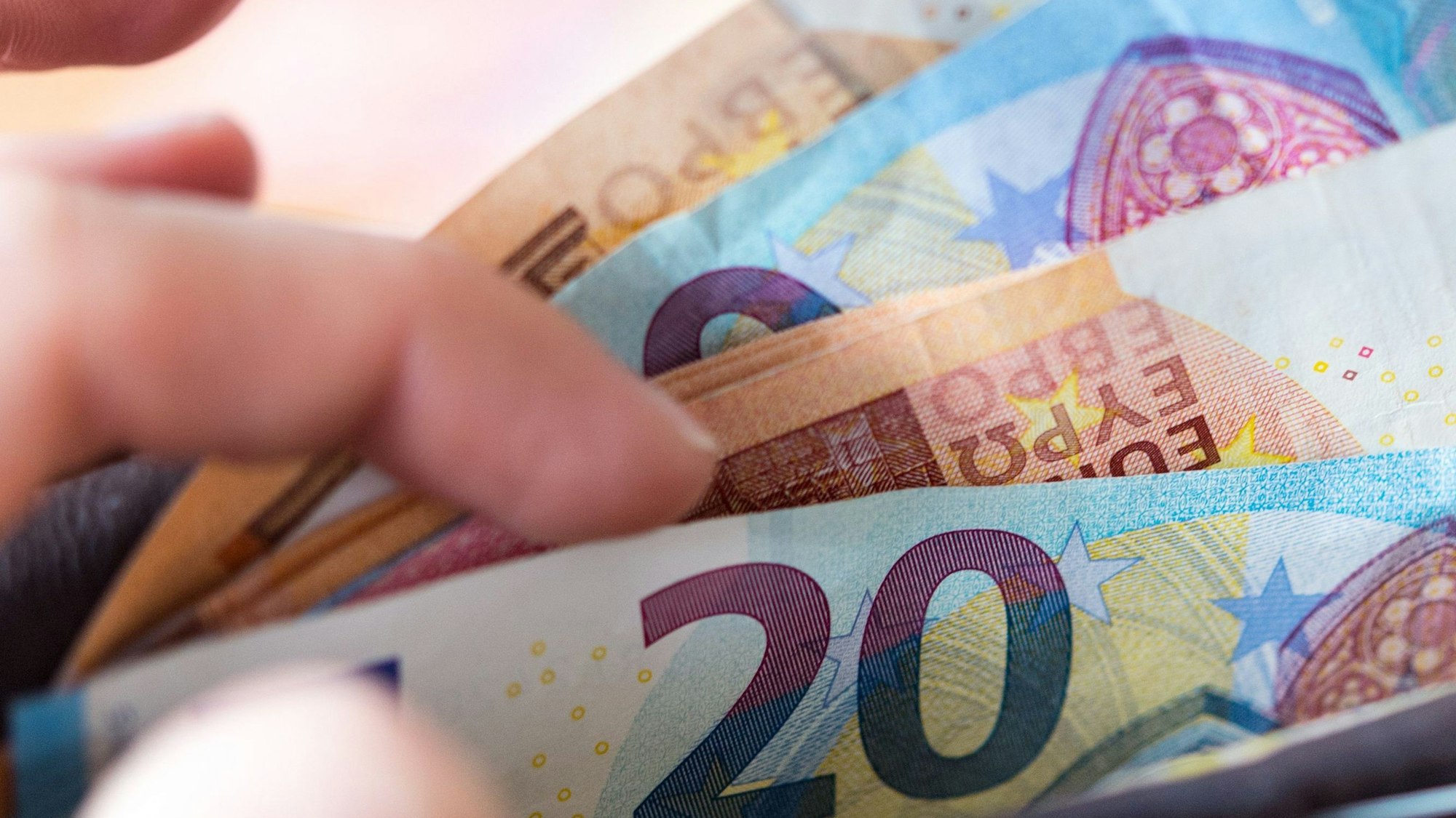 Eine Frau hält eine Geldbörse mit Banknoten in der Hand und zieht einen 20-Euro-Schein heraus.