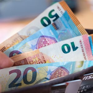 Eine Frau hält eine Geldbörse mit Banknoten in der Hand und zieht einen 20-Euro-Schein heraus.