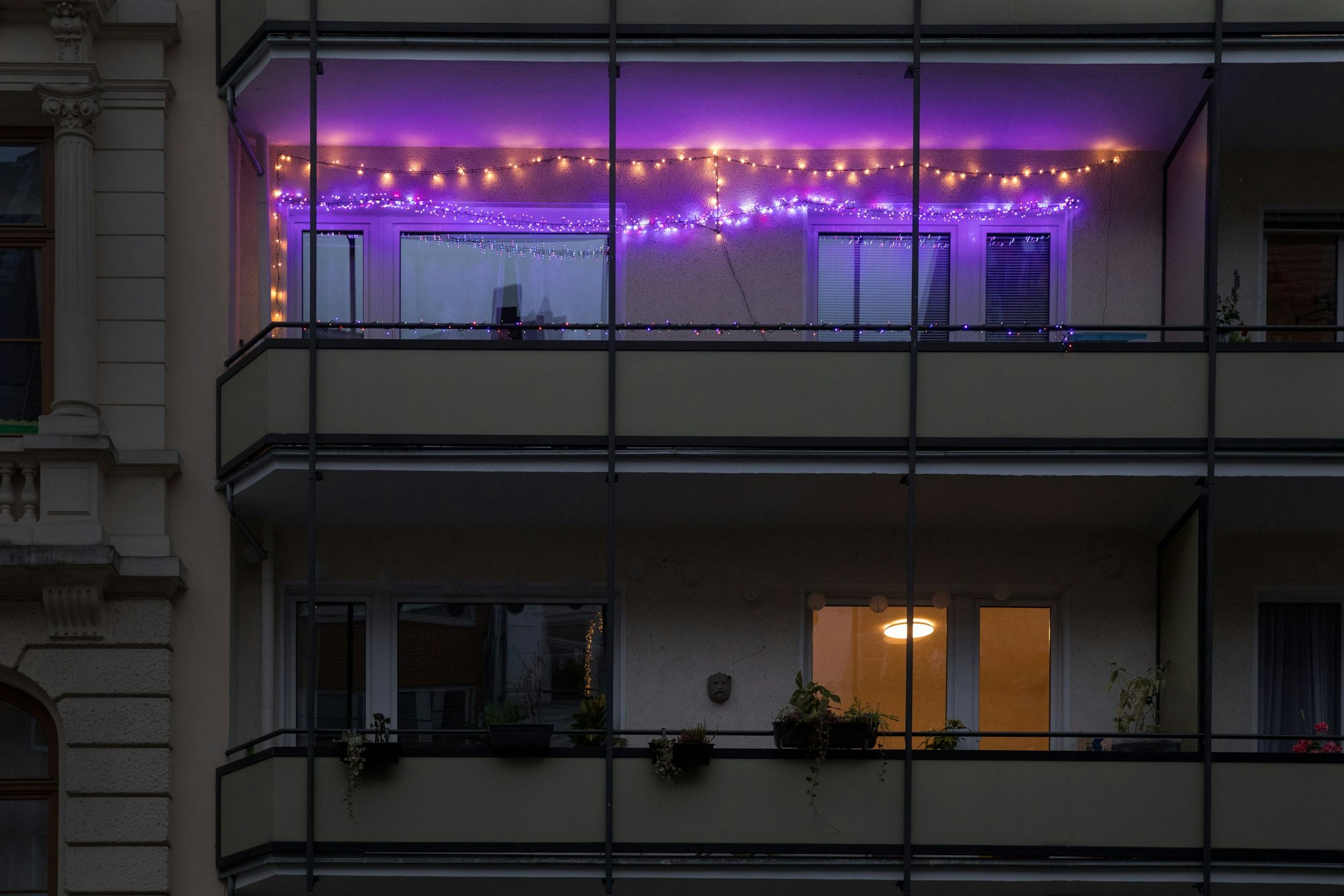 Zwei Lichterketten hängen an einem Balkon. Eine leuchtet in warmweißer Farbe, die zweite in violett.