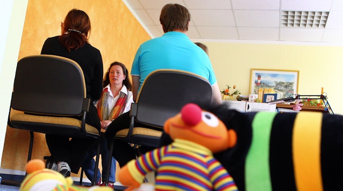 Eine Familie nimmt in einer Beratungsstelle k an einer Erziehungsberatung mit Psychologin Birgit Höppner teil. Im Vordergrund liegen Plüschfiguren aus der Sesamstraße