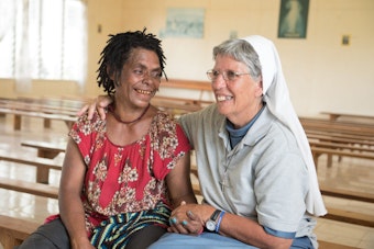 Die Ordensschwester Lorena Jenal sitzt mit der Überlebenden einer Hexenverbrennung in Papua Neuguinea in einer Kirche in Kundiawa und hält ihre Hand.