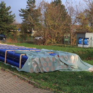 Die neuen blauen Abwasserrohre liegen bereits auf einer Wiese neben der Straße bereit.