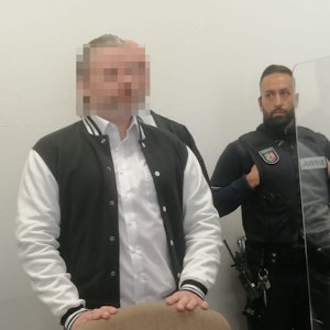 Das Foto zeigt das unkenntlich gemachte Gesicht des Angeklagten. Neben ihn steht ein Justizvollzugsbeamter.