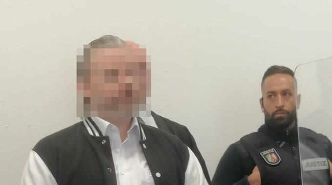 Das Foto zeigt das unkenntlich gemachte Gesicht des Angeklagten. Neben ihn steht ein Justizvollzugsbeamter.