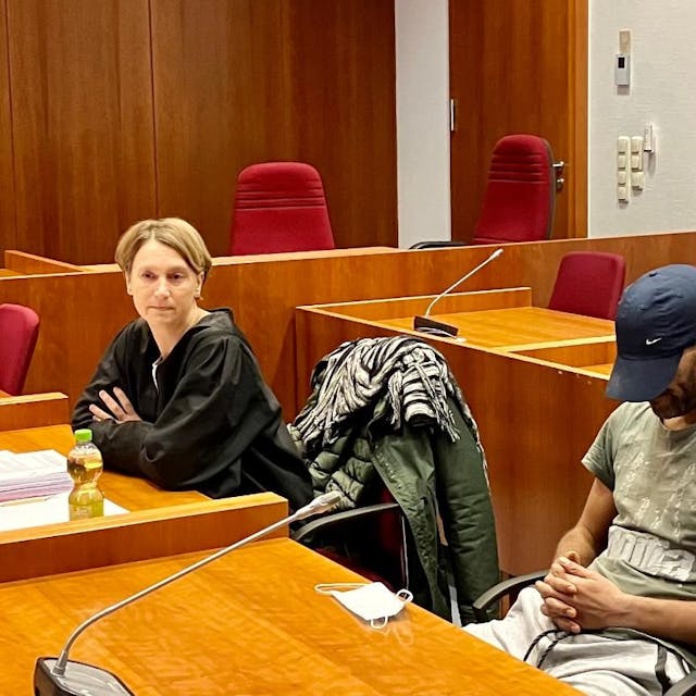Ein Angeklagter sitzt neben seiner Verteidigerin im Gerichtssaal. Er trägt eine Baseballmütze tief ins Gesicht gezogen.