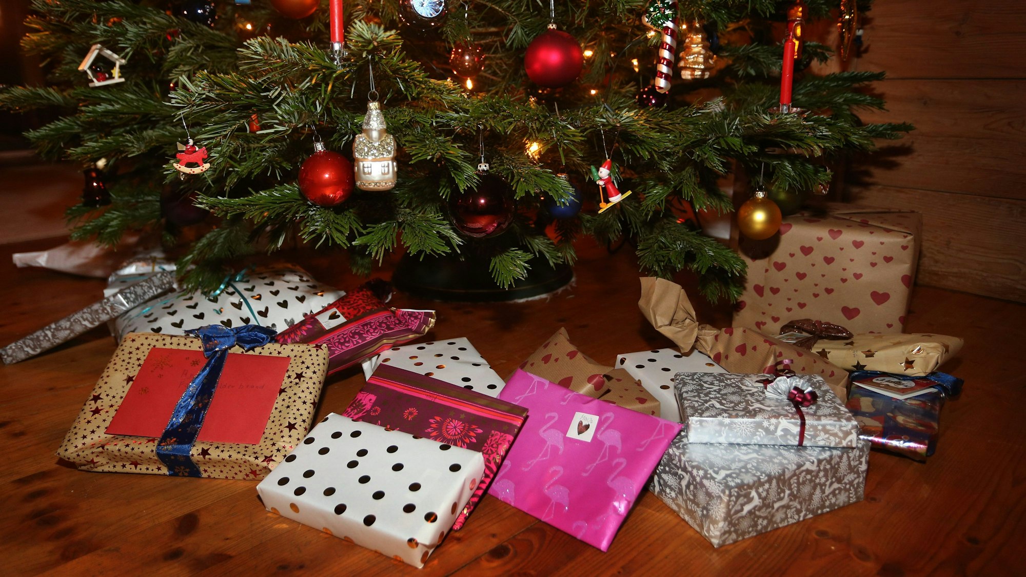 Verpackte Weihnachtsgeschenke liegen in einem Wohnzimmer unter einem geschmückten Weihnachtsbaum.