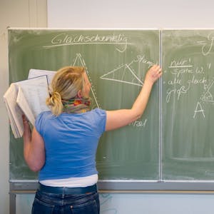 Eine Lehrerin schreibt mit Kreide an die Tafel.