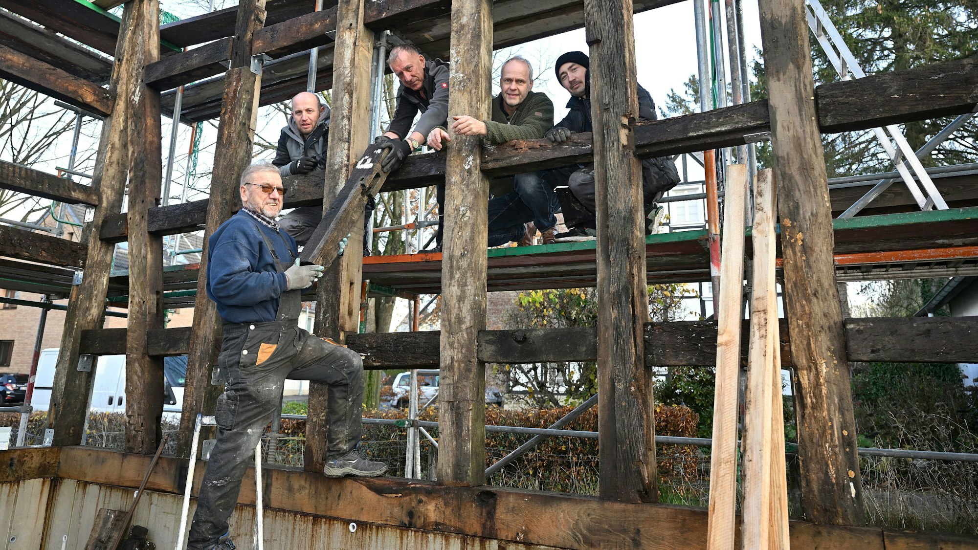 Markus Hetzenegger steht mit vier weiteren Handwerkern zwischen den Holzbalken eines noch unfertigen Fachwerkhauses.