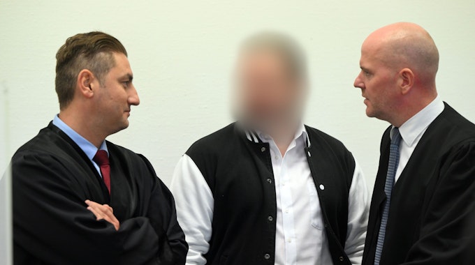 Der Angeklagte steht zwischen seinen Anwälten im Kölner Landgericht.