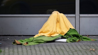 Ein Obdachloser hat sich zum Schutz vor Kälte mehrere Decken um seinen Körper gewickelt.