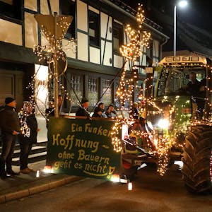 Ein grüner, ganz besonders mit Lichtern geschmückter Traktor fährt ein Schild mit der Aufschrift „Ein Funken Hoffnung – Ohne Bauern geht es nicht“ durch Overath.