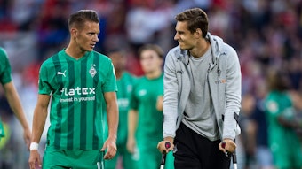 Hannes Wolf spricht mit seinem Teamkollegen Florian Neuhaus von Borussia Mönchengladbach, der wegen einer Verletzung auf Krücken ist.