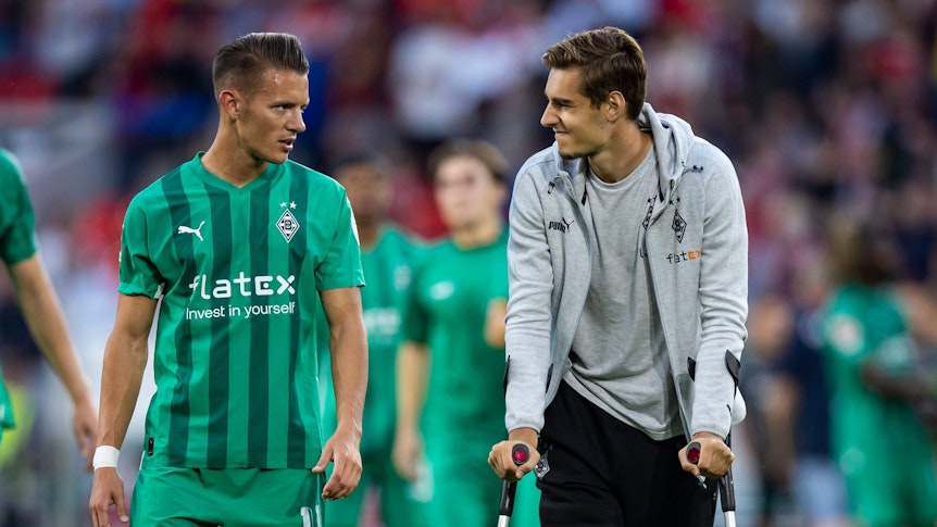 Hannes Wolf spricht mit seinem Teamkollegen Florian Neuhaus von Borussia Mönchengladbach, der wegen einer Verletzung auf Krücken ist.