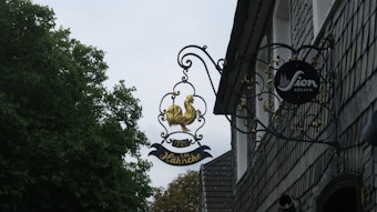 Das Eingangsschild des Gasthauses "Em Hähnche" in Brück zeigt einen goldenen Hahn.