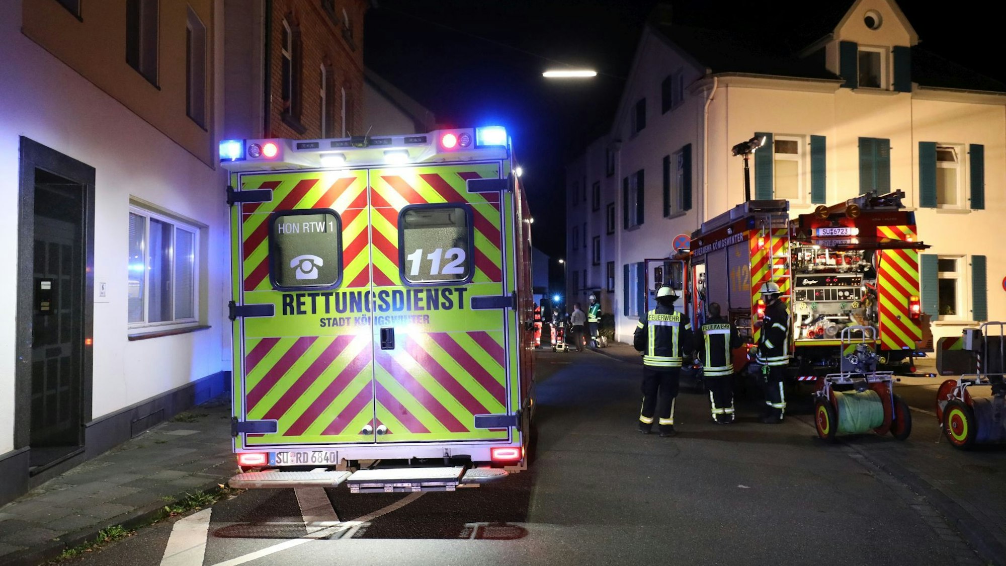 Ein Einsatzwagen des Rettungsdienstes steht nachts in einer Wohnstraße, im Hintergrund sind auch ein Fahrzeug der Feuerwehr und Feuerwehrleute zu sehen.