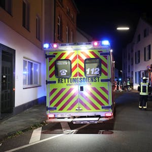 Ein Einsatzwagen des Rettungsdienstes steht nachts in einer Wohnstraße, im Hintergrund sind auch ein Fahrzeug der Feuerwehr und Feuerwehrleute zu sehen.&nbsp;