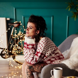 Junge Frau sitzt traurig im Weihnachtspullover vor einer Lichterkette.