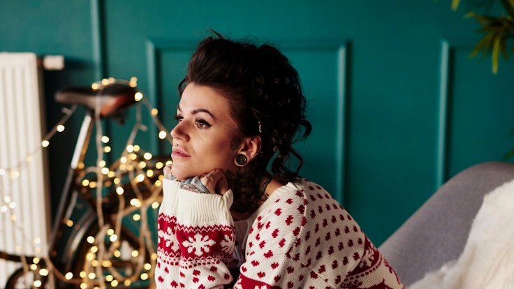 Junge Frau sitzt traurig im Weihnachtspullover vor einer Lichterkette.