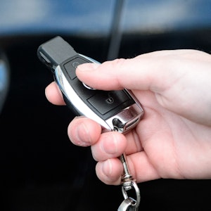 Eine Person hält einen Autoschlüssel in der Hand. Im Hintergrund ist das Fahrzeug zu sehen.