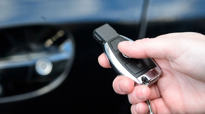 Eine Person hält einen Autoschlüssel in der Hand. Im Hintergrund ist das Fahrzeug zu sehen.