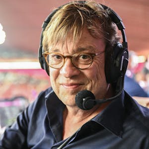 Fußball-Kommentator Béla Réthy sitzt vor einer Übertragung der Fußball-Weltmeisterschaft 2022 in Katar im Stadion an seinem Kommentatorenplatz. Er trägt ein Headset mit Mikrofon.