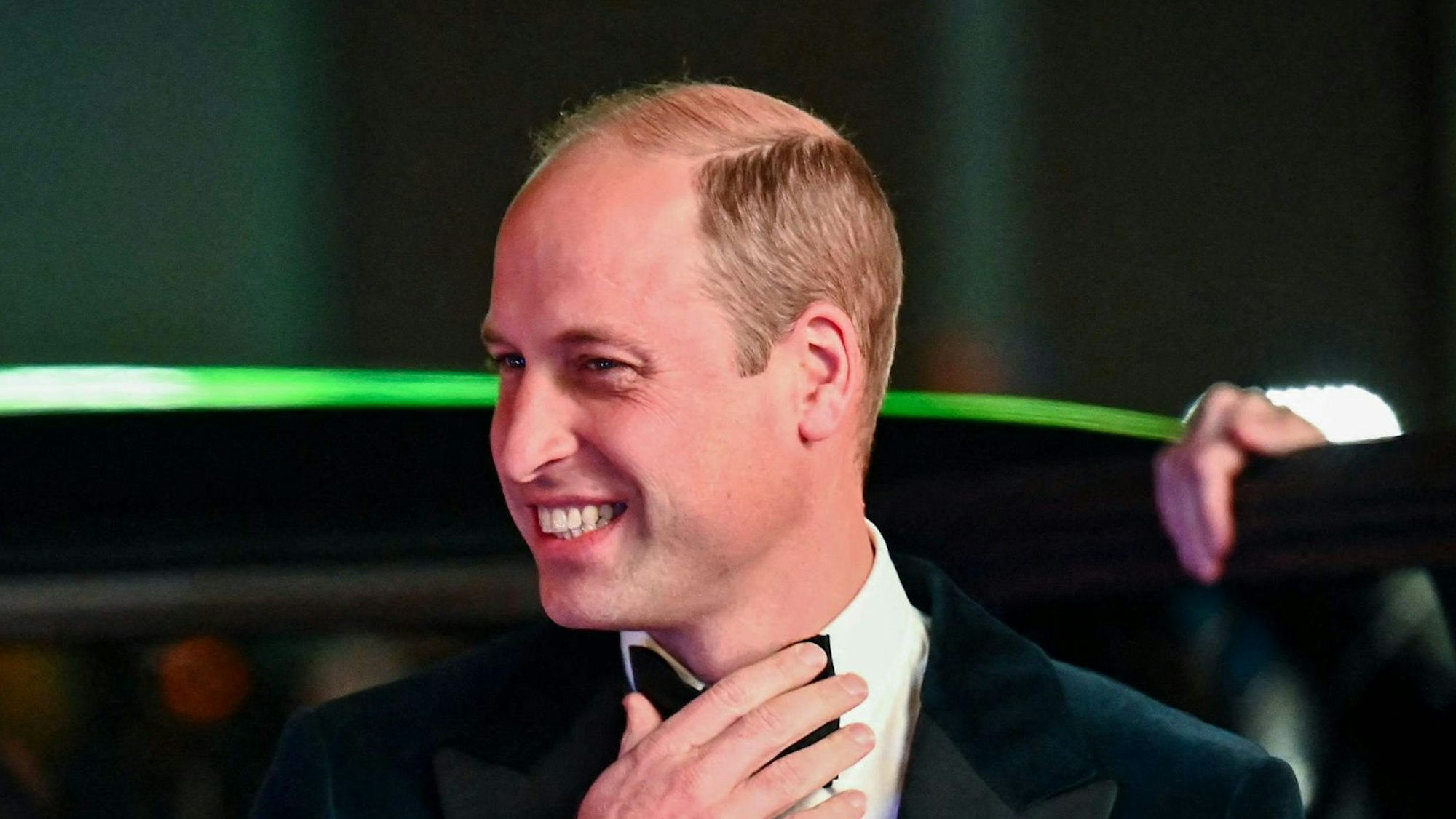 Prinz William mit Fliege und Anzug. Er grinst und steigt aus einem Auto.