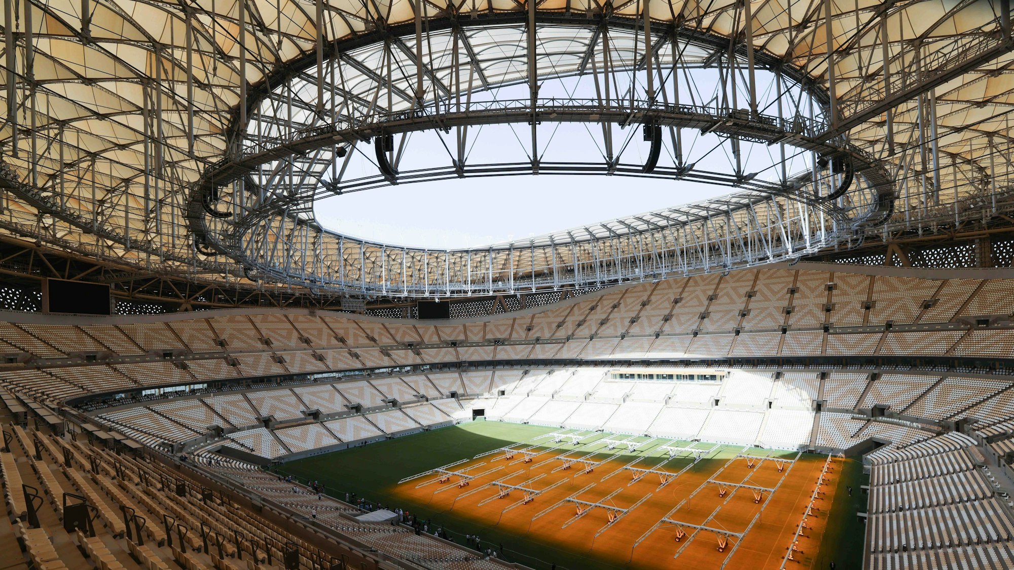 Zu sehen ist das Innere des Fußballstadions, von oben aus einer Tribüne fotografiert. Es ist Tag und die Sonne scheint in das Stadion.
