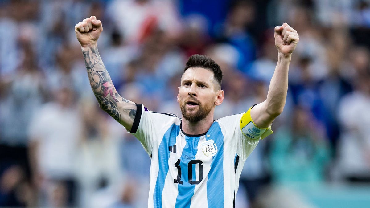 Lionel Messi steht im Trikot von Argentinien mit der Nr. 10 vor der Kurve und reckt beide Fäuste in die Höhe.